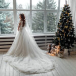 bride standing in front of window next to christmas tree