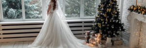 bride standing in front of window next to christmas tree