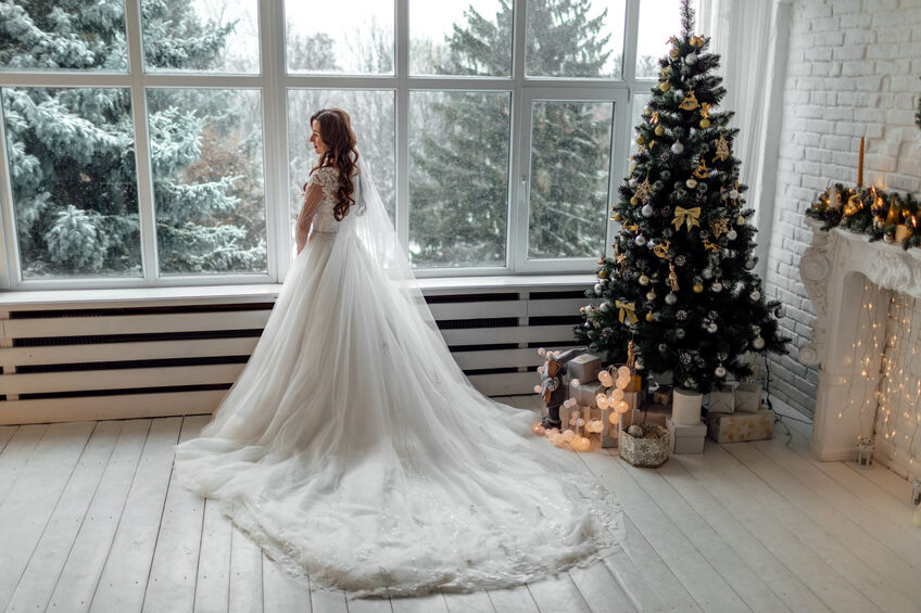 bride standing in front of window next to christmas tree